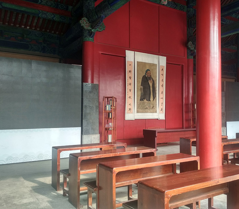 Pupitres de 1920 dentro del templo. En la pared del fondo, una de las pinturas más famosas que representan al maestro Kong, Confucio. Foto: Exterior del recinto del Templo de Confucio en Qufu. Foto, Shizhao, Patios interiores del templo de la familia Kong en Qufu. Foto: Diego Tiriria, Relieve en piedra de Confucio en el templo dedicado a su memoria en Qufu. Foto: Diego Titiria, Wikimedia commons, dominio público para «Qufu Confucian Temple».