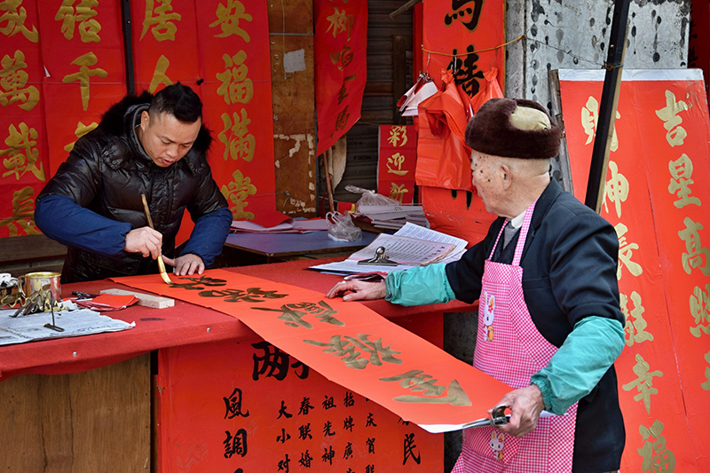 Fiesta de la Primavera. Los chun lian se pueden comprar en los mercados, realizados por expertos calígrafos. Estos, en el mercado de Foshan, están escribiendo coplas de primavera ("chun lian" en chino) para la celebración del Año Nuevo Chino. El significado de los caracteres es bendición, eterna felicidad. Foto: 123RF.